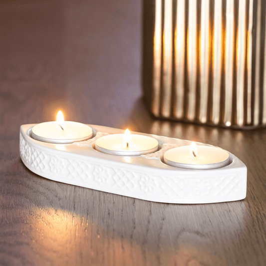 White ceramic candle holder with three lit candles on a wooden surface.