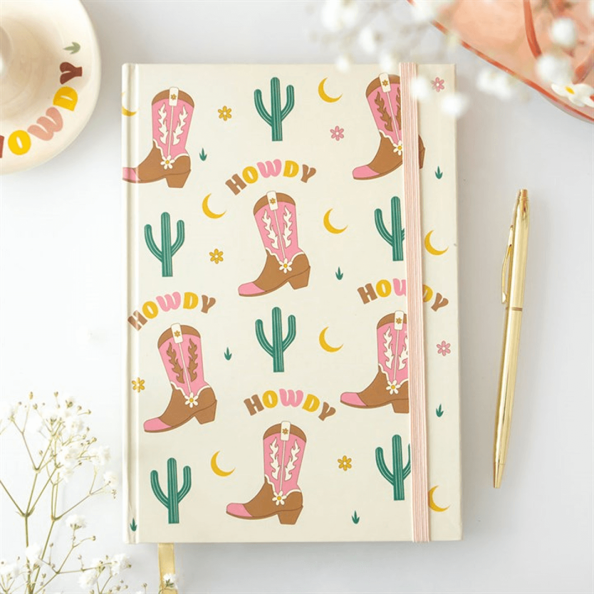 Notebook with cowboy boot and cactus pattern on a white surface with a pen and decorative items.