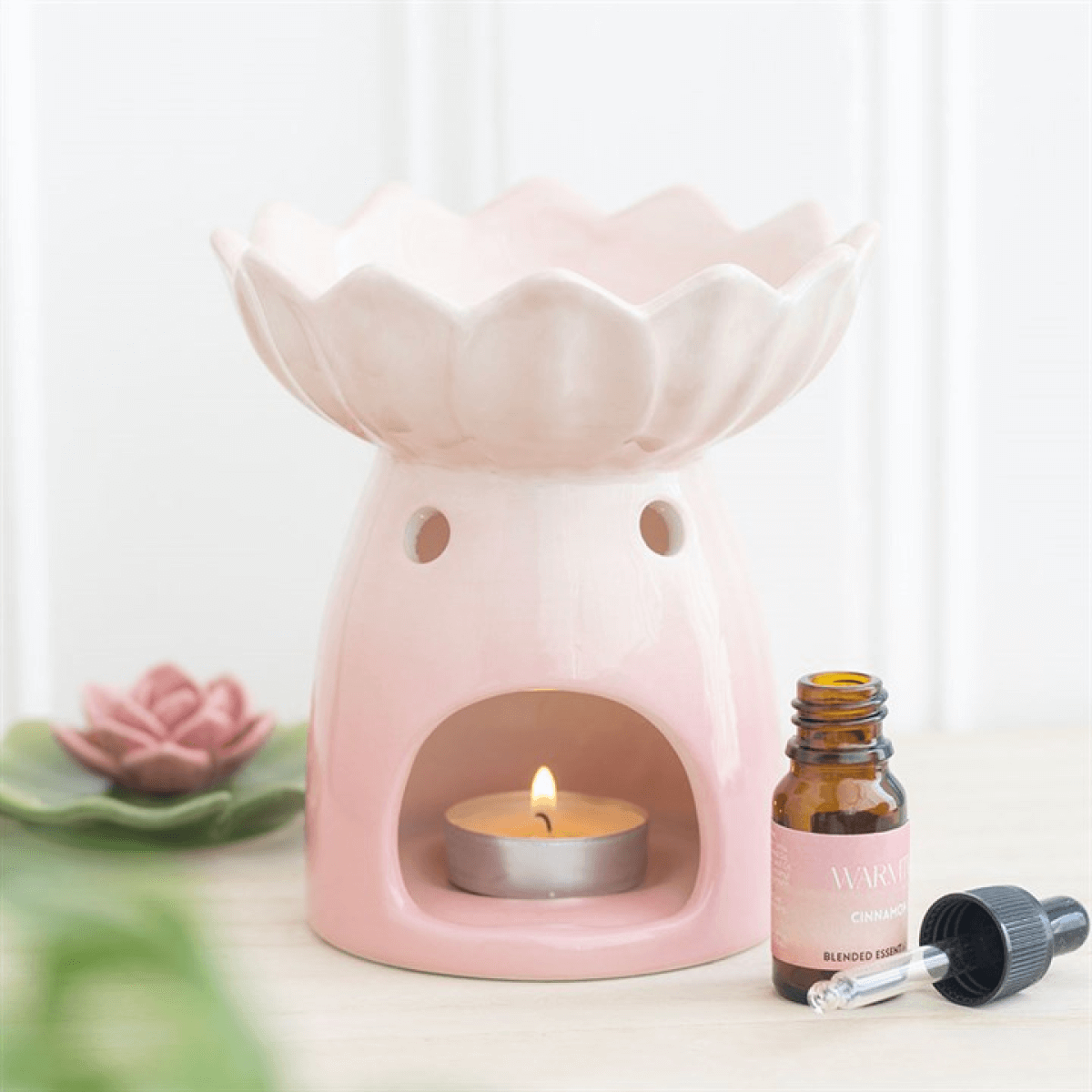 Pink ceramic oil burner with a lit candle and essential oil bottle on a white background