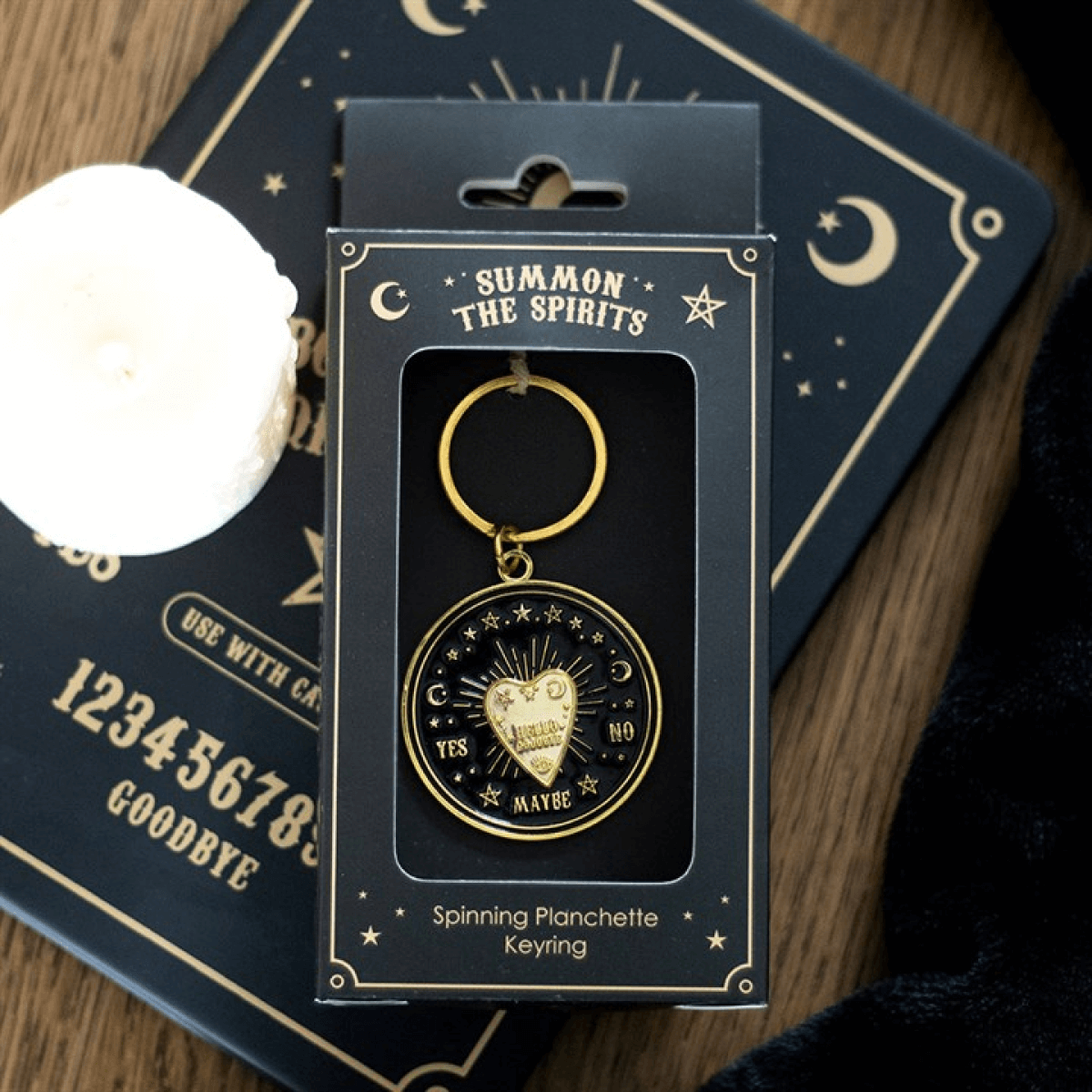 Gold keychain with a spinning planchette design in packaging labeled 'Summon the Spirits'.