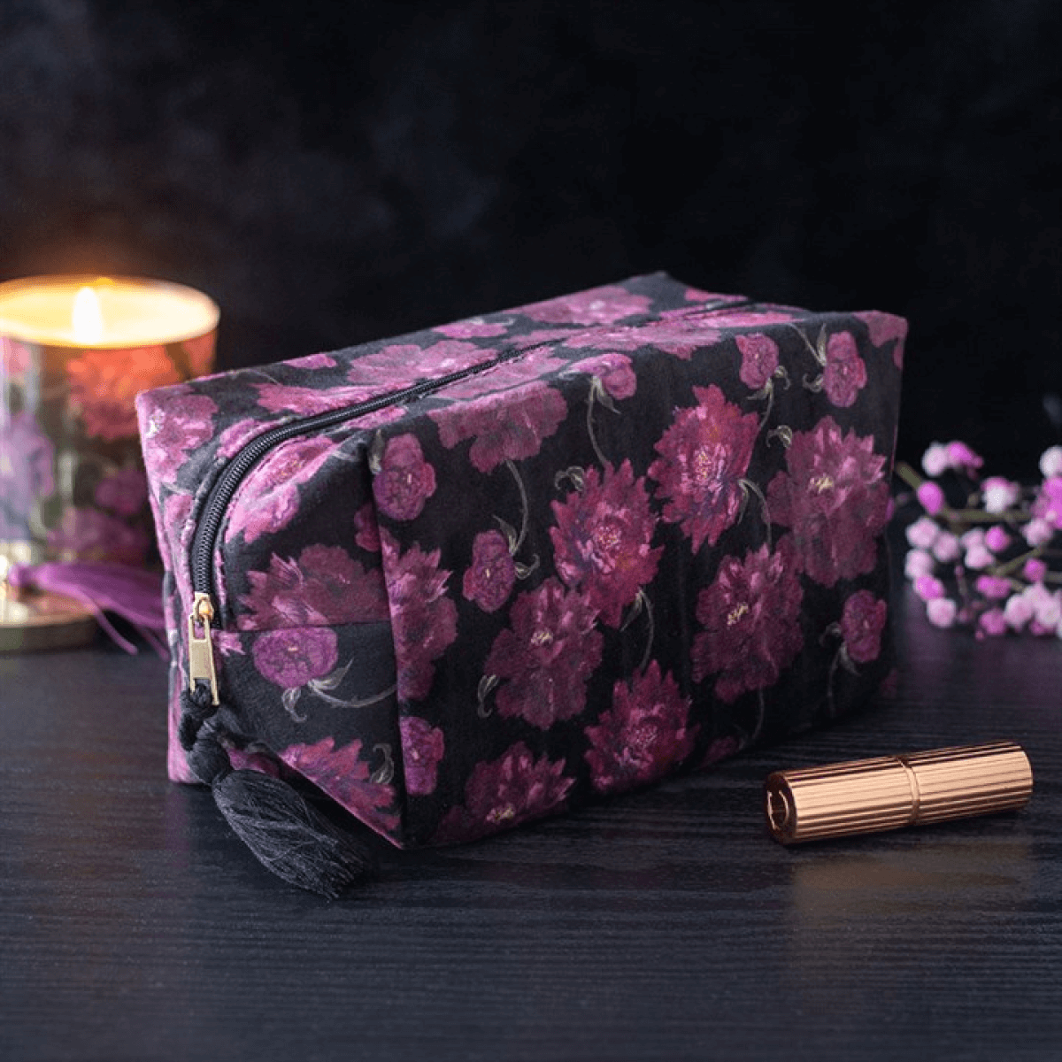 Floral patterned makeup bag on a dark surface with a candle and flowers in the background