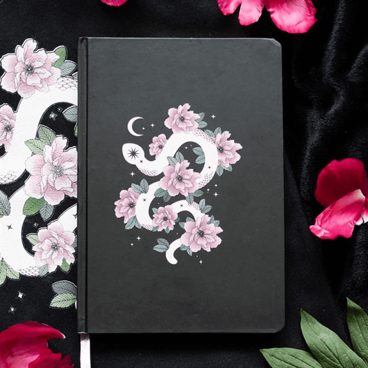 Black notebook with floral and snake design on a dark background with flowers.