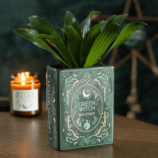 Green Witch book of spells with a lit candle on a wooden surface