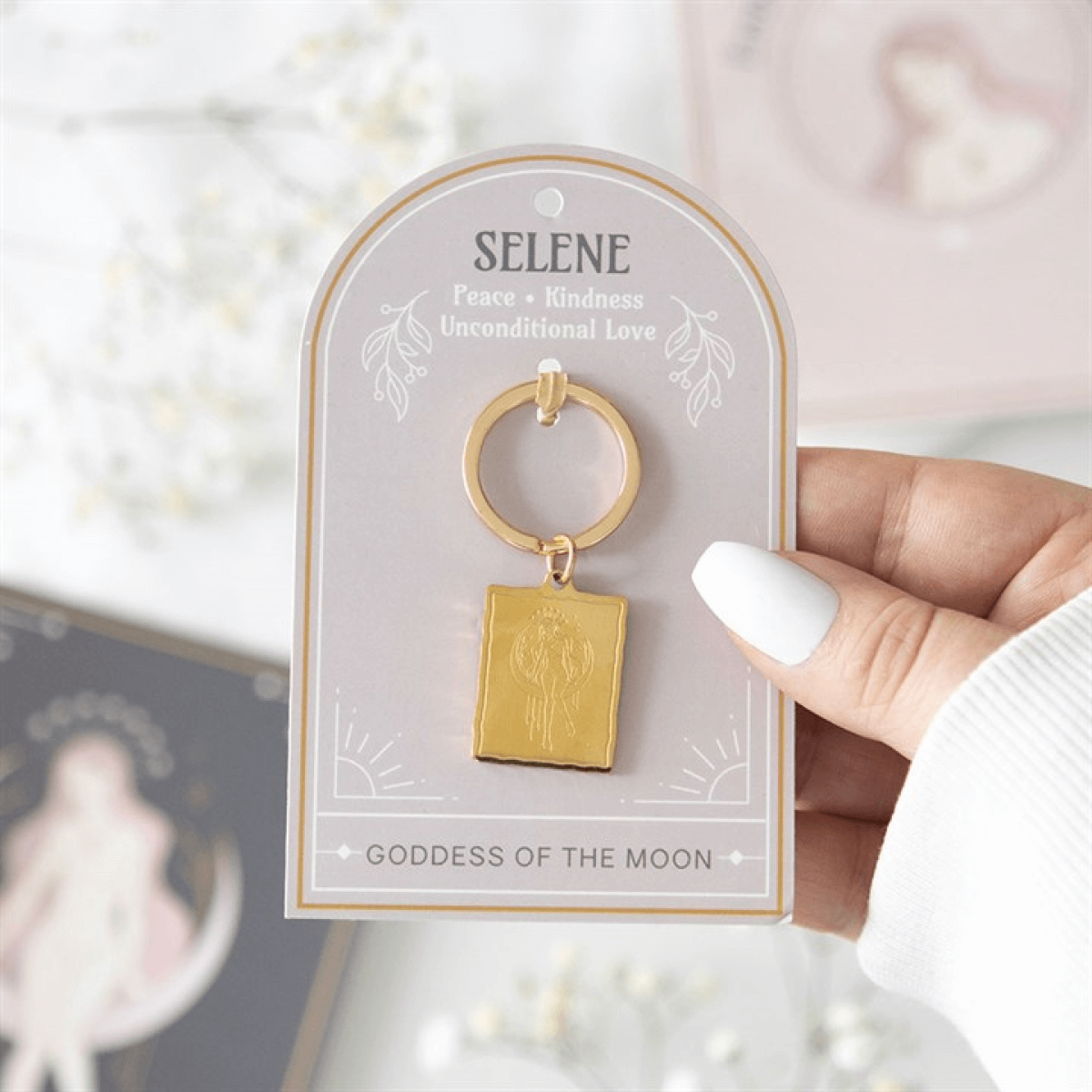 Gold keychain on a Selene branded card held by a hand with white nail polish.