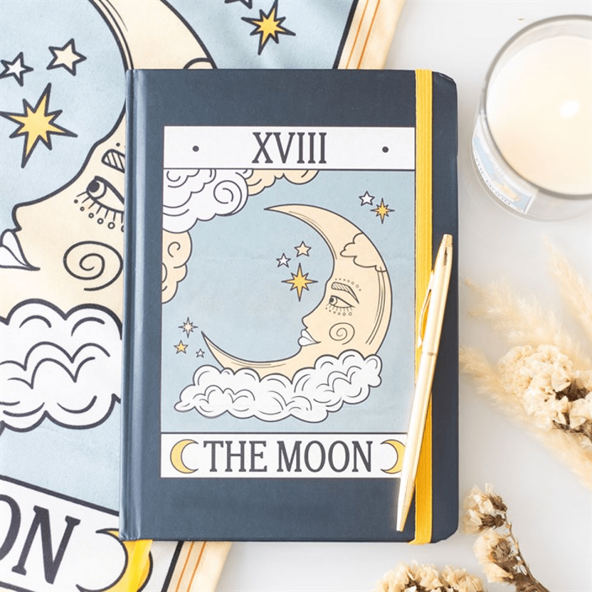 Notebook with 'The Moon' tarot card design on a table with candles and crystals.