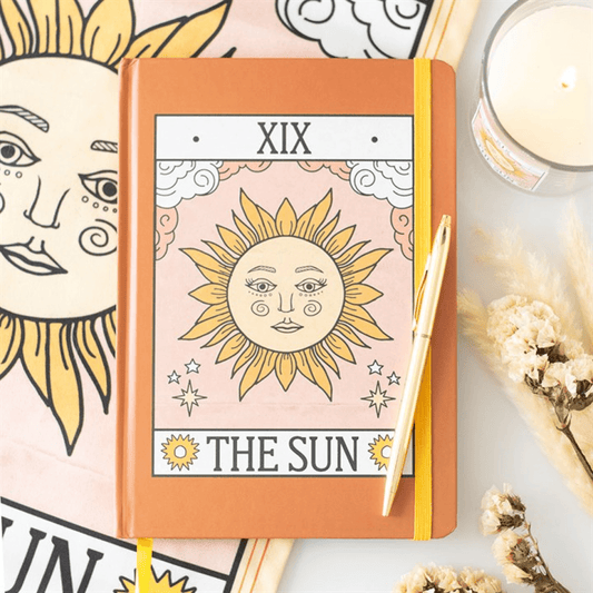 Notebook with 'The Sun' tarot card design on a decorative background with candles and flowers.