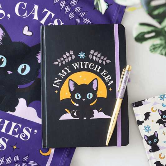 Black notebook with a cat illustration and 'In my witch era' text, surrounded by decorative items.