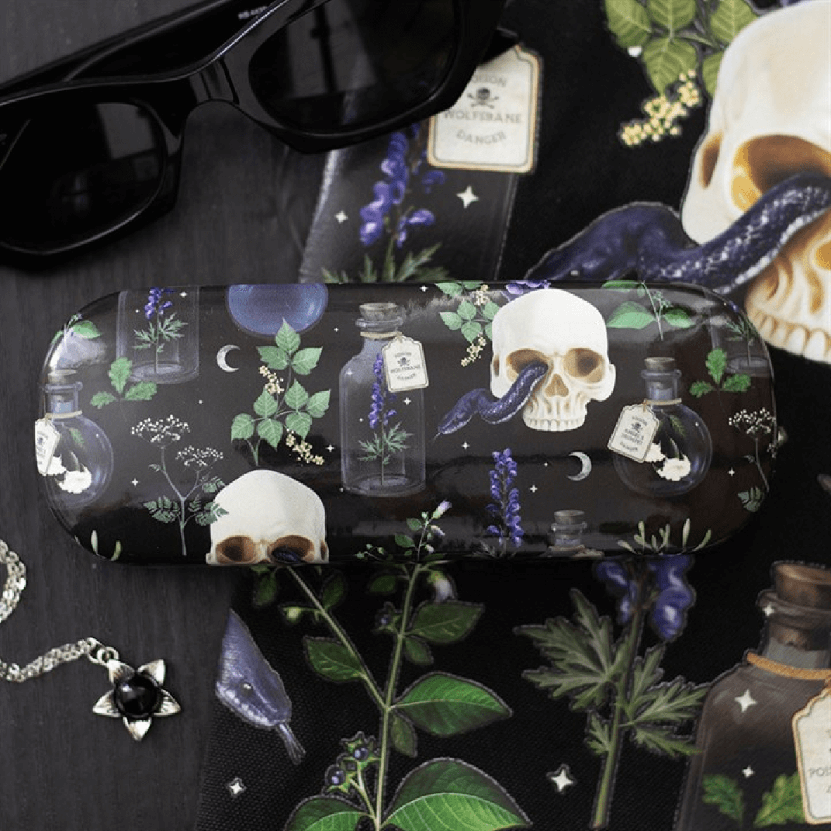 Sunglasses on a black surface with a decorative case featuring skulls, bottles, and plants.
