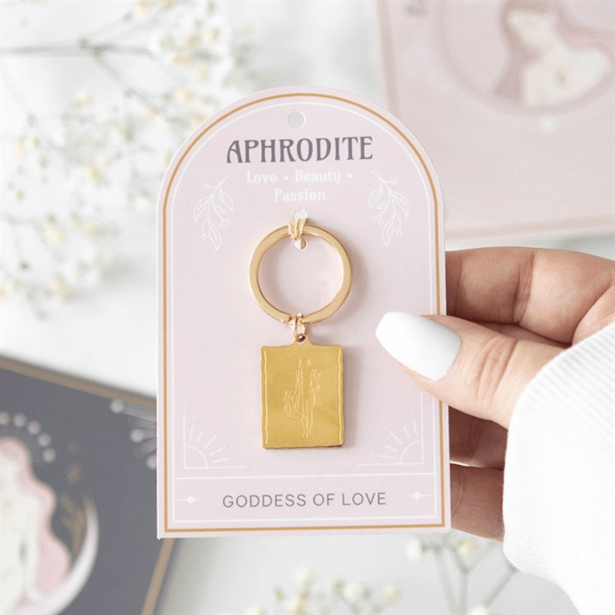 Gold keychain on a 'Aphrodite' branded card held by a hand.