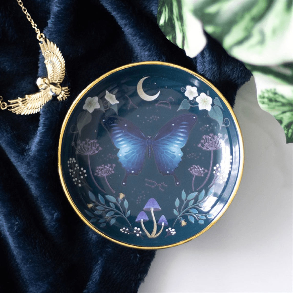 Round Midnight Moth Trinket Dish with a blue moth design and gold edging on a dark background.