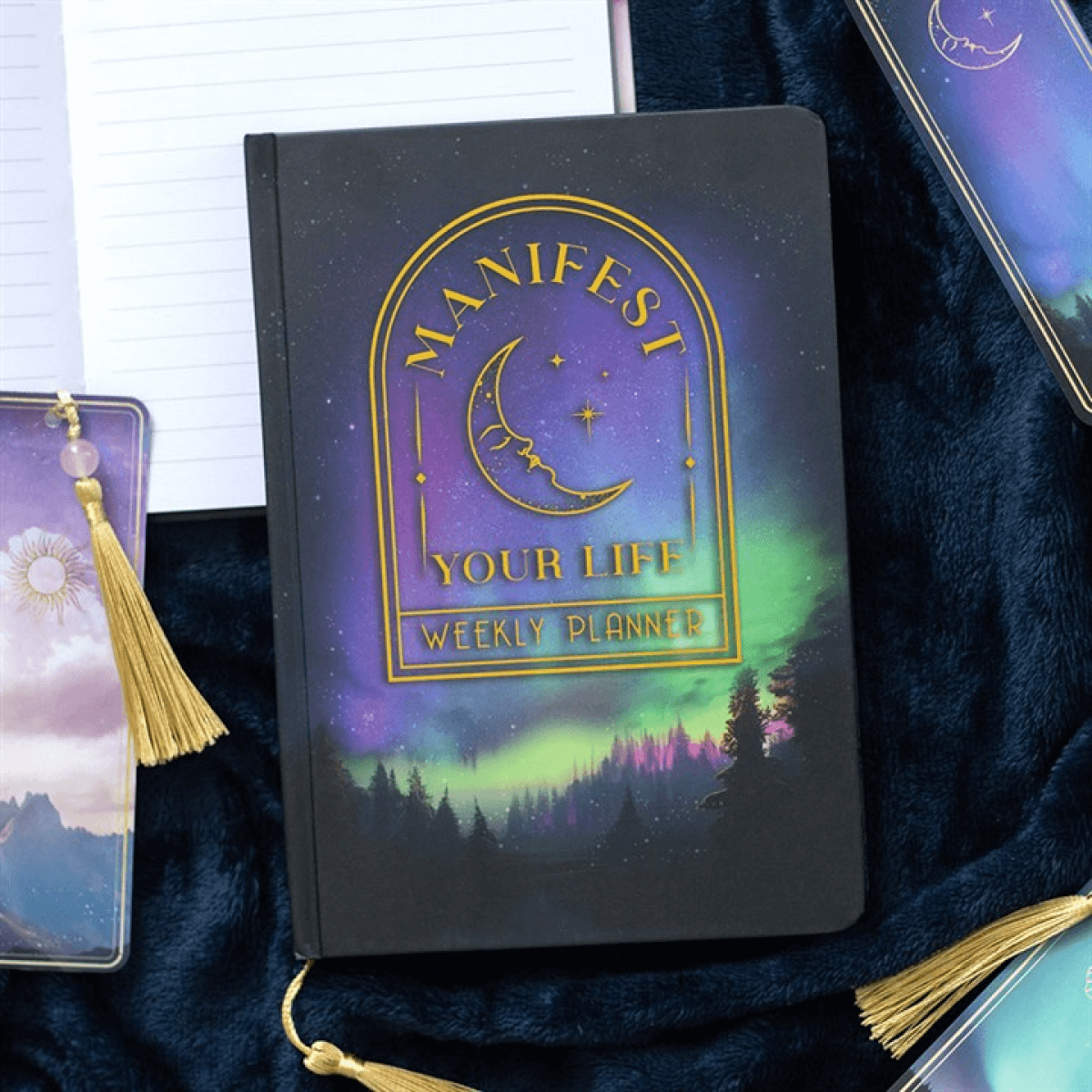 Weekly planner with 'Manifest Your Life' design on a dark surface with tarot cards and a phone.