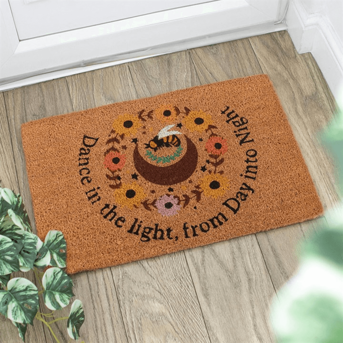 Decorative doormat with floral design and text on a wooden floor.